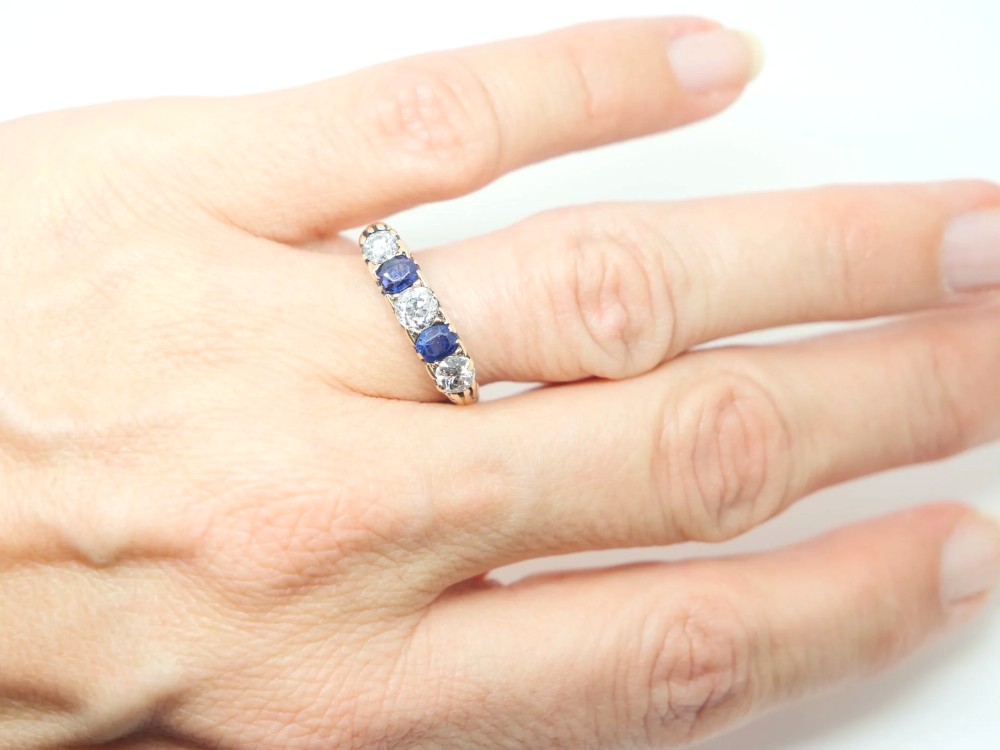 An 18ct yellow gold five-stone ring set with alternating round diamonds and oval blue sapphires in claw mounts. View IV