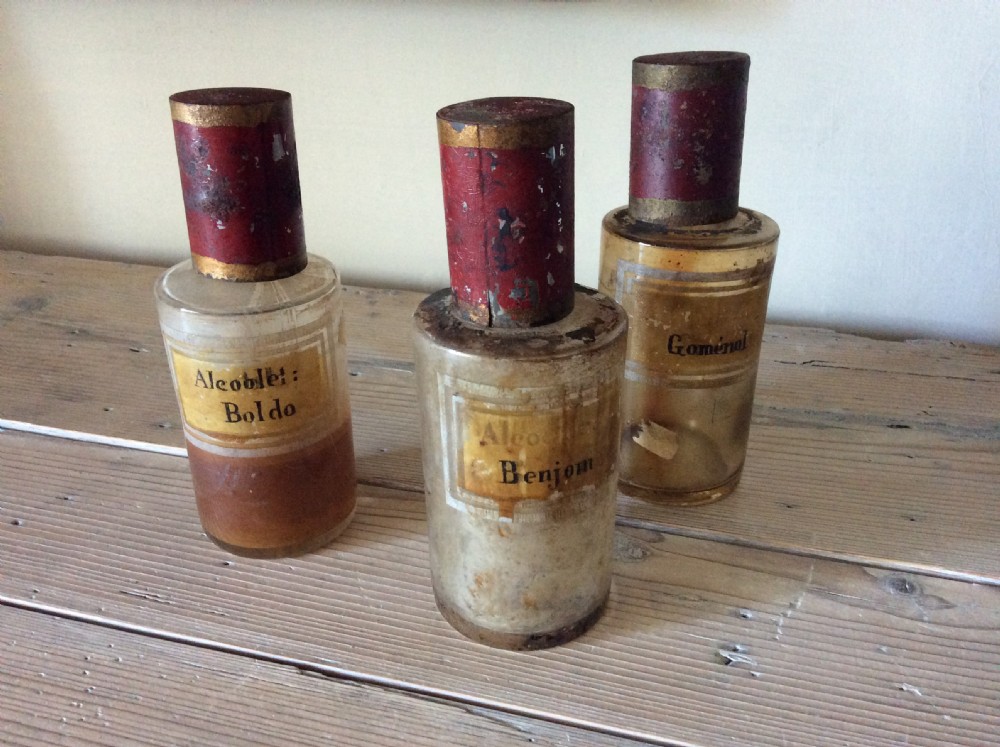 A trio of 19th-century cylindrical glass apothecary bottles featuring original French paper labels and red paint with gold trim stoppers.
