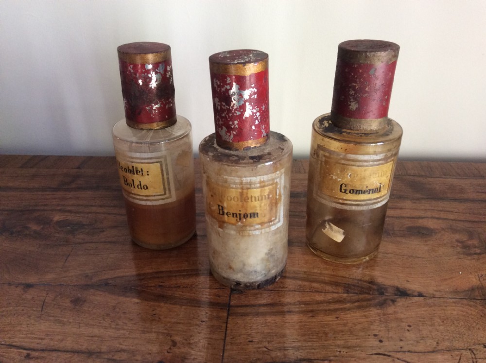 A trio of 19th-century cylindrical glass apothecary bottles featuring original French paper labels and red paint with gold trim stoppers. View II