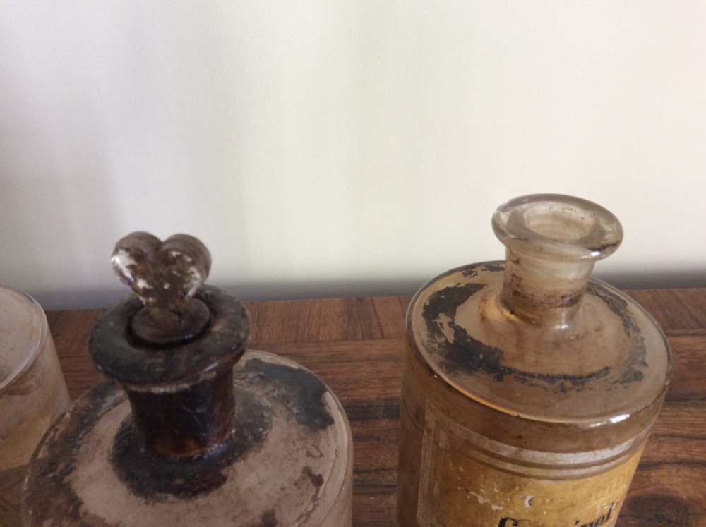 A trio of 19th-century cylindrical glass apothecary bottles featuring original French paper labels and red paint with gold trim stoppers. View IV