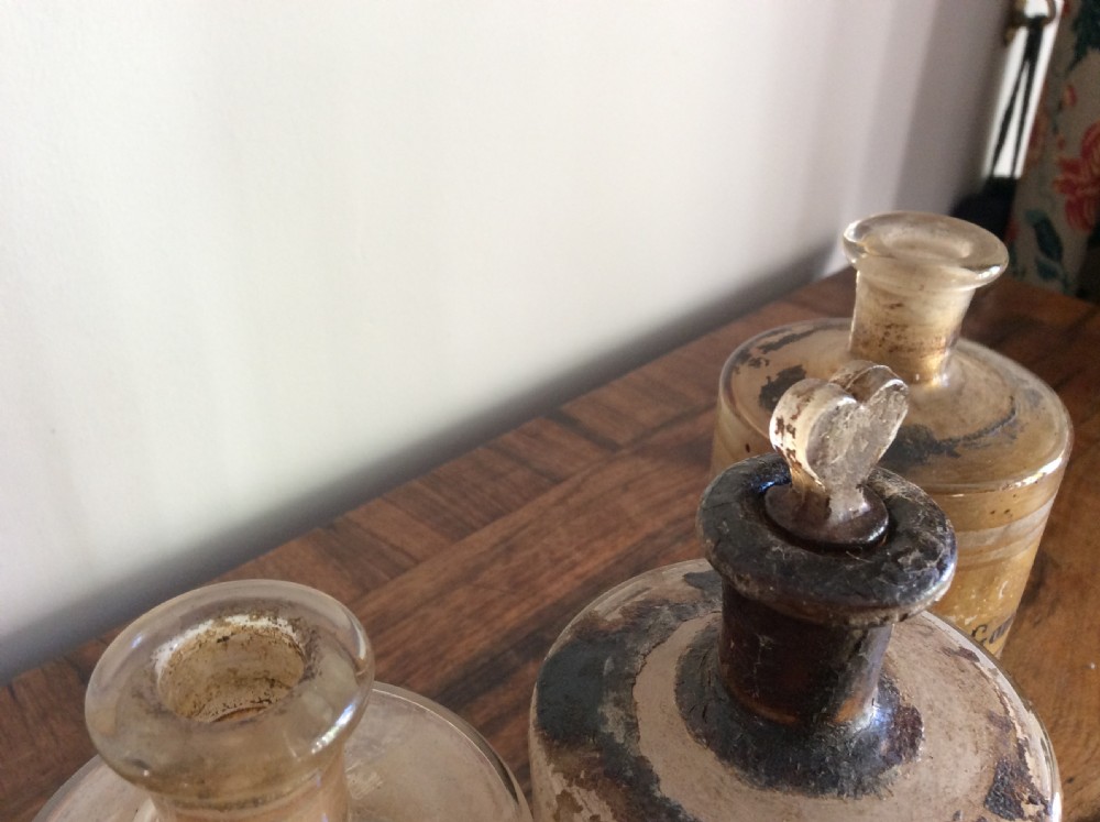 A trio of 19th-century cylindrical glass apothecary bottles featuring original French paper labels and red paint with gold trim stoppers. View V