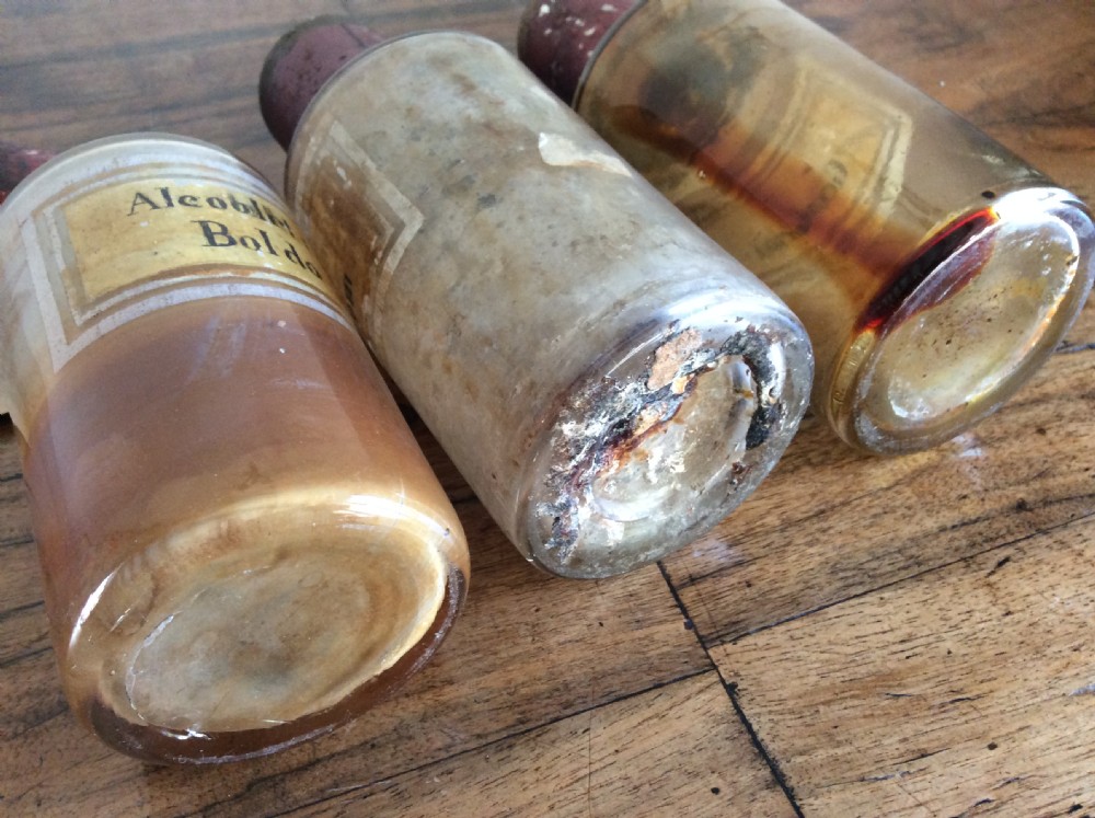 A trio of 19th-century cylindrical glass apothecary bottles featuring original French paper labels and red paint with gold trim stoppers. View VI