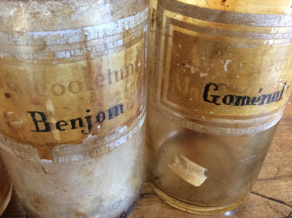 A trio of 19th-century cylindrical glass apothecary bottles featuring original French paper labels and red paint with gold trim stoppers. View VII