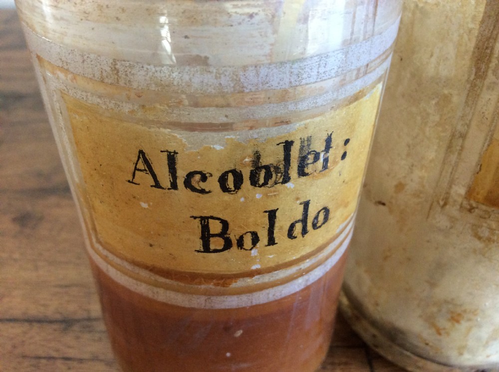 A trio of 19th-century cylindrical glass apothecary bottles featuring original French paper labels and red paint with gold trim stoppers. View VIII