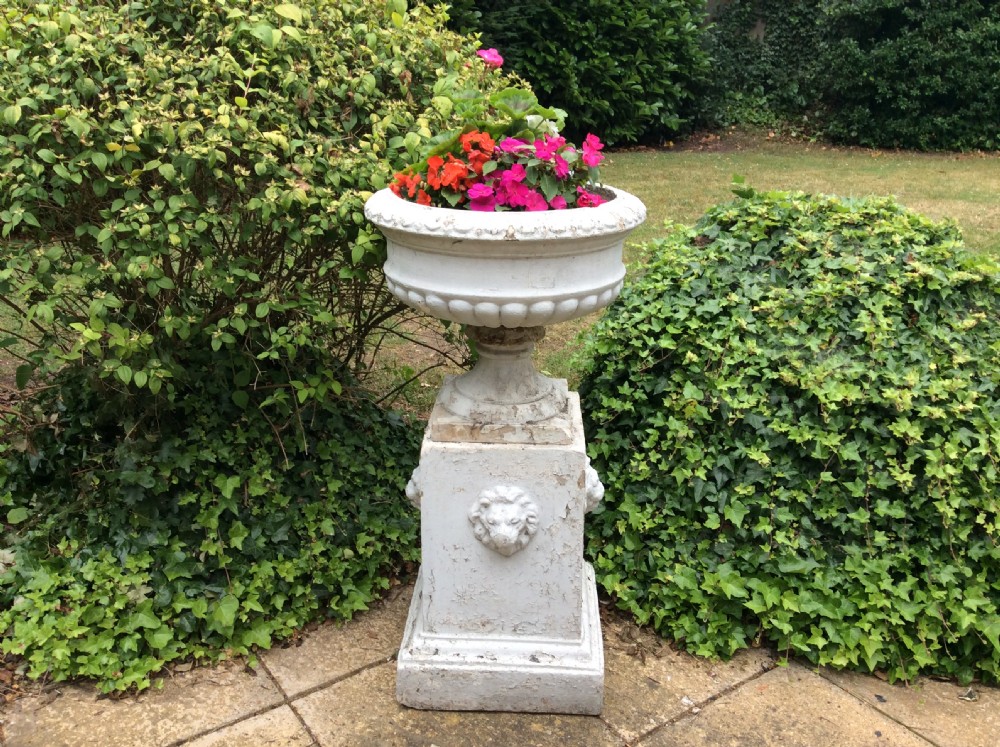 A pair of white painted 19th-century cast iron garden urns featuring gadrooned basins set upon square pedestals with lion head relief motifs. View V