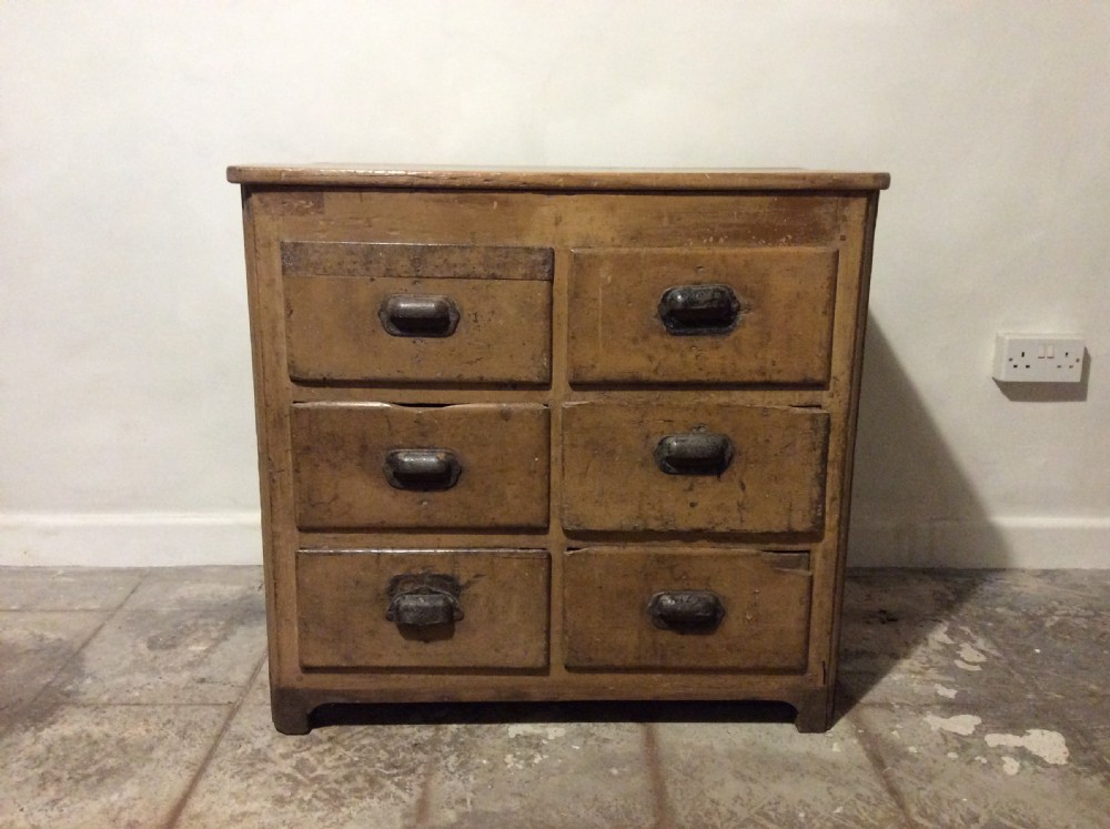 A natural pine French chest of six drawers featuring dark metal shell cup handles arranged in two vertical columns.