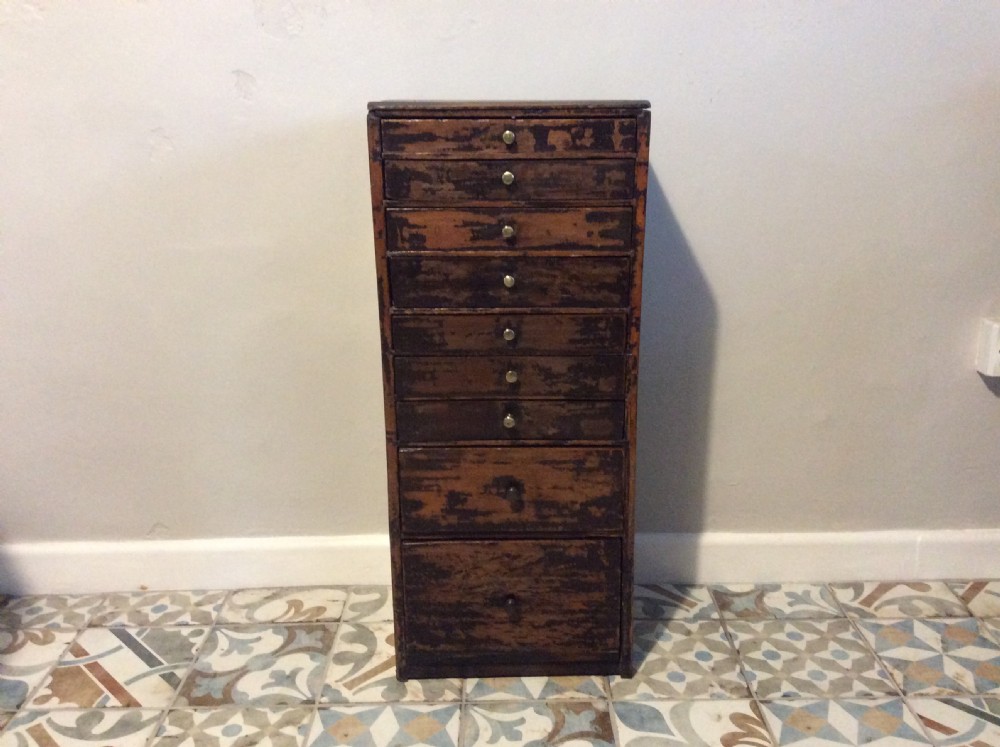 A tall and narrow dark brown wooden chest featuring nine graduated drawers with small brass knobs and a distressed finish.