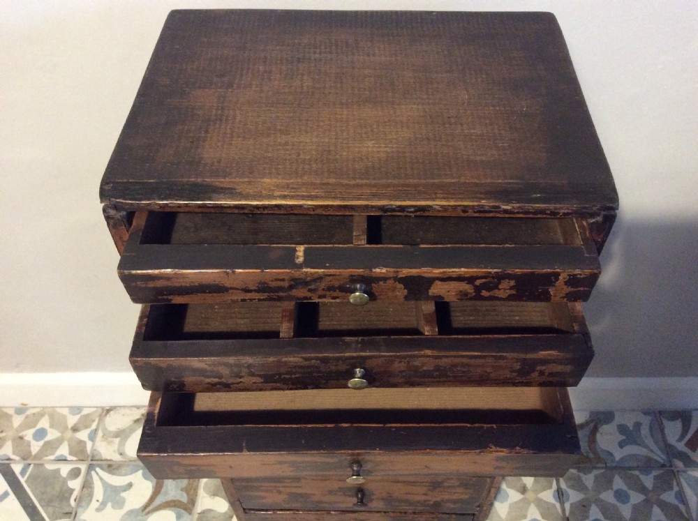A tall and narrow dark brown wooden chest featuring nine graduated drawers with small brass knobs and a distressed finish. View III
