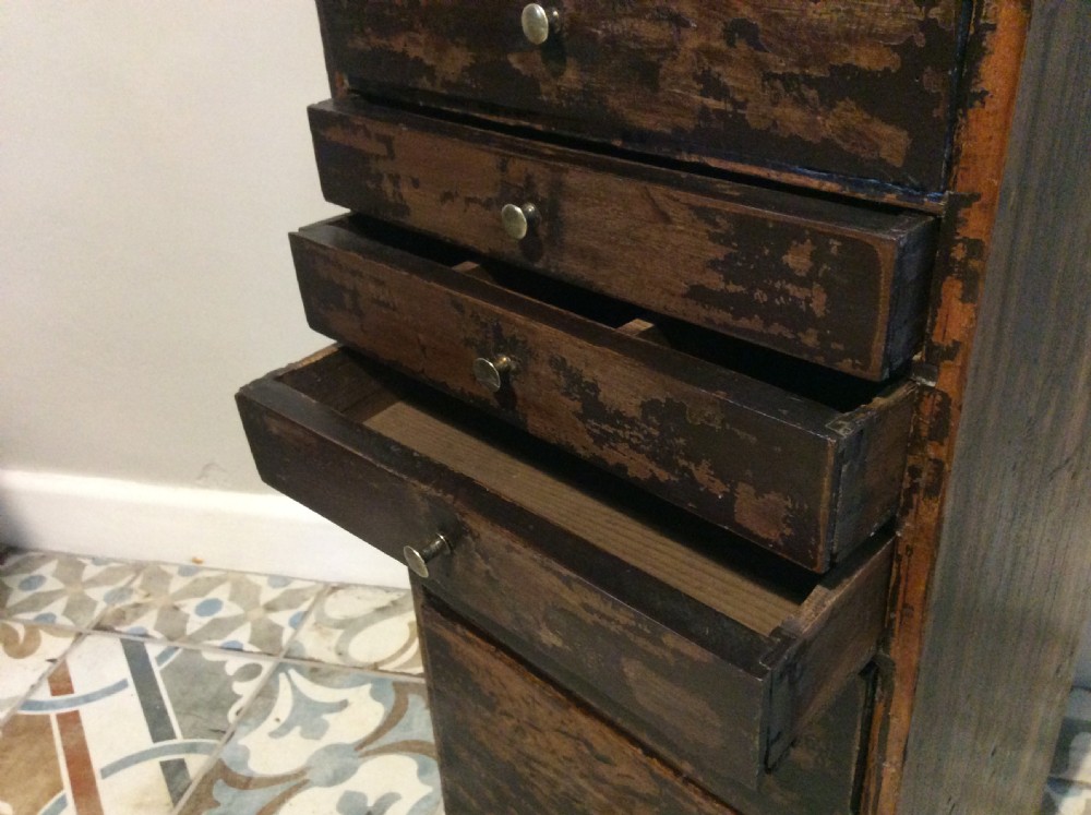 A tall and narrow dark brown wooden chest featuring nine graduated drawers with small brass knobs and a distressed finish. View IX
