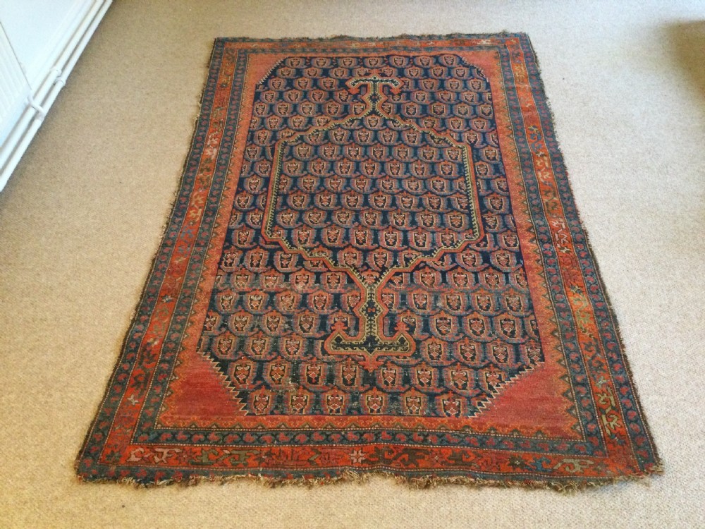 An antique hand-knotted Caucasian prayer rug displaying a central mihrab arch and repeating geometric motifs in terracotta, indigo, and navy wool.