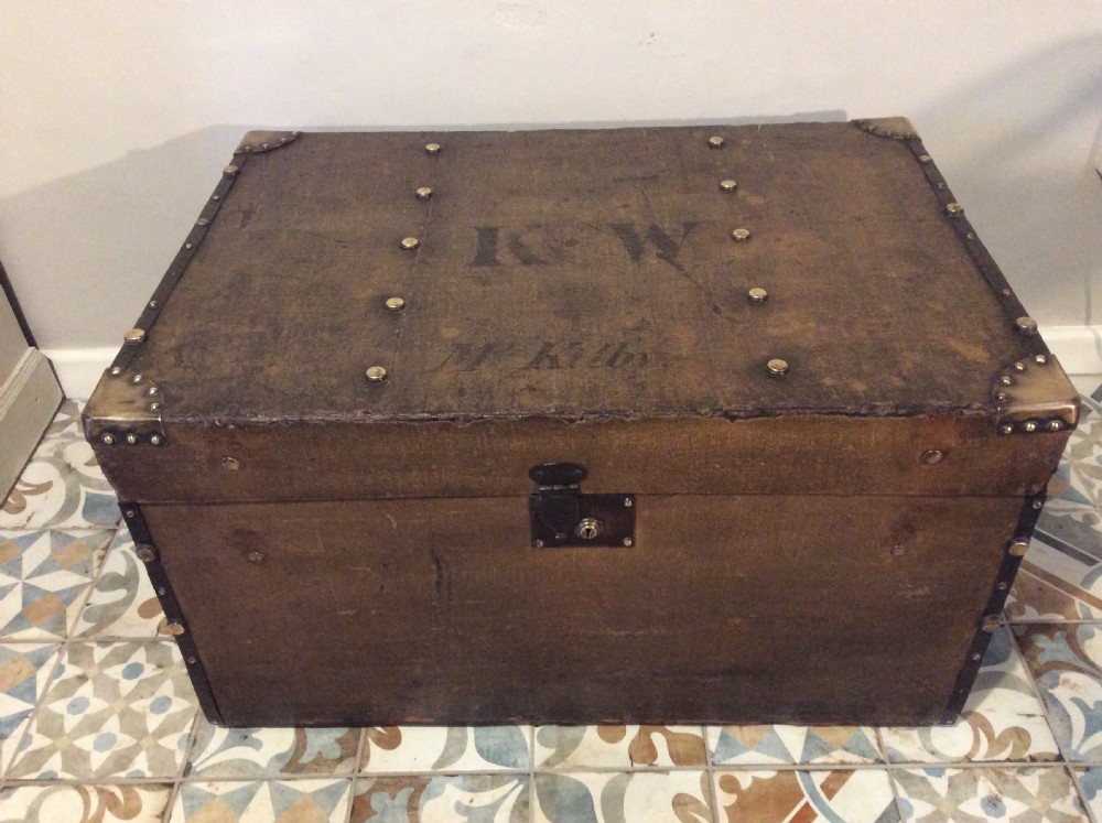 A rectangular Victorian dark brown canvas-covered trunk featuring brass corner caps, brass studs, a central lock, and stencilled black initials on the flat lid.