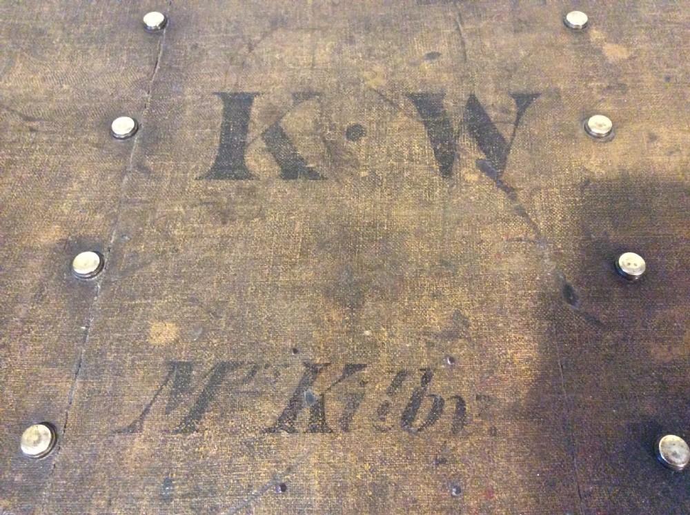 A rectangular Victorian dark brown canvas-covered trunk featuring brass corner caps, brass studs, a central lock, and stencilled black initials on the flat lid. View III