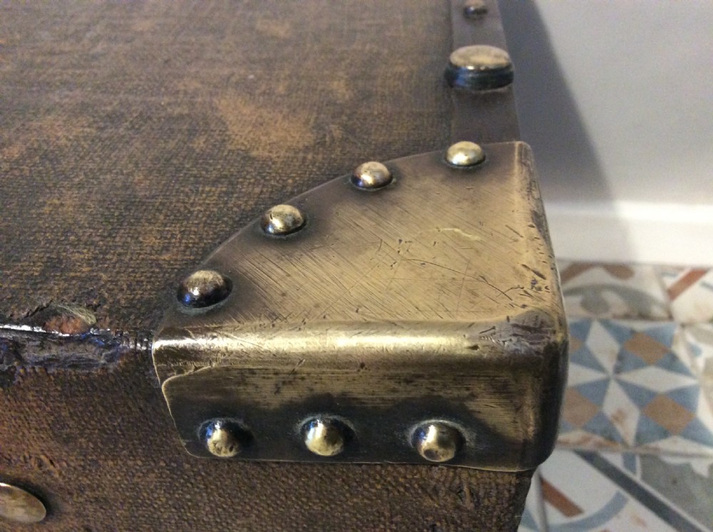 A rectangular Victorian dark brown canvas-covered trunk featuring brass corner caps, brass studs, a central lock, and stencilled black initials on the flat lid. View IX