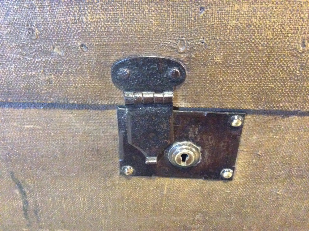 A rectangular Victorian dark brown canvas-covered trunk featuring brass corner caps, brass studs, a central lock, and stencilled black initials on the flat lid. View XII