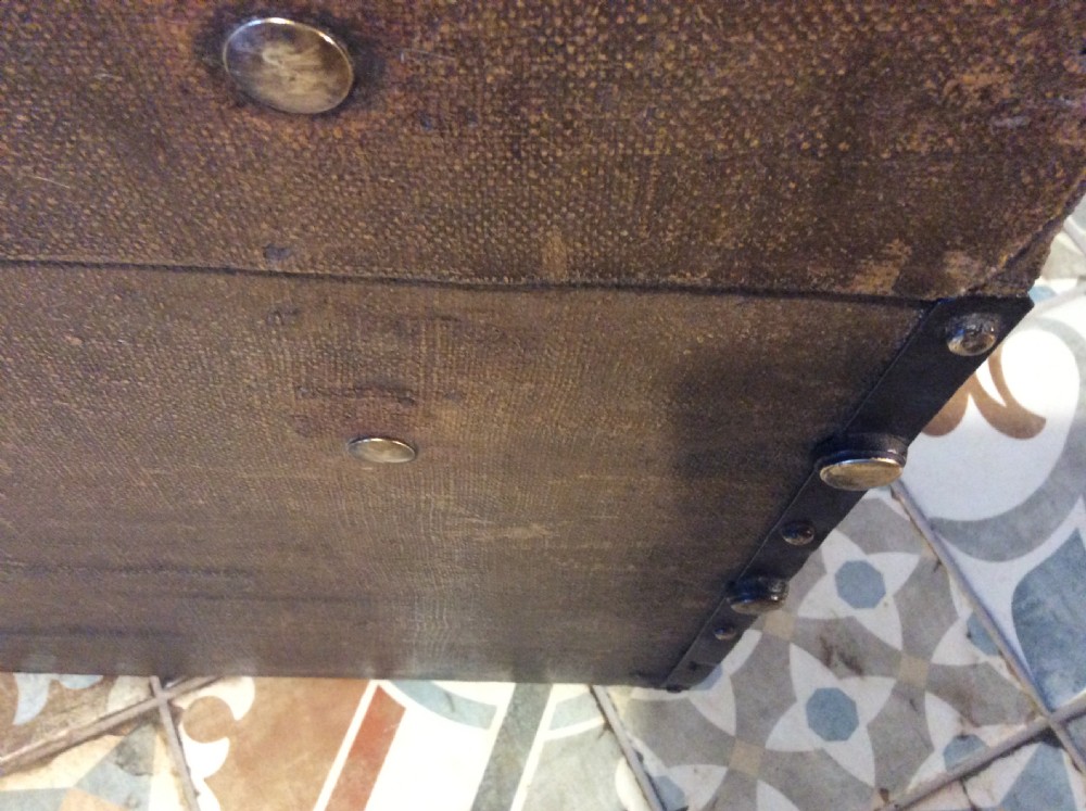 A rectangular Victorian dark brown canvas-covered trunk featuring brass corner caps, brass studs, a central lock, and stencilled black initials on the flat lid. View XIII
