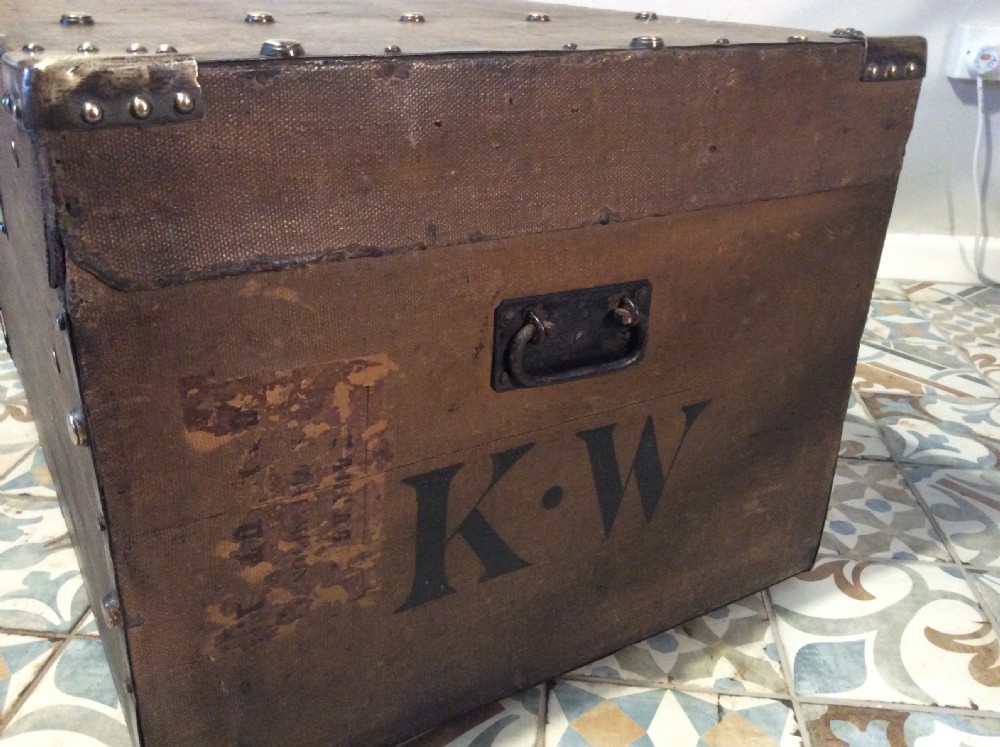 A rectangular Victorian dark brown canvas-covered trunk featuring brass corner caps, brass studs, a central lock, and stencilled black initials on the flat lid. View XIV