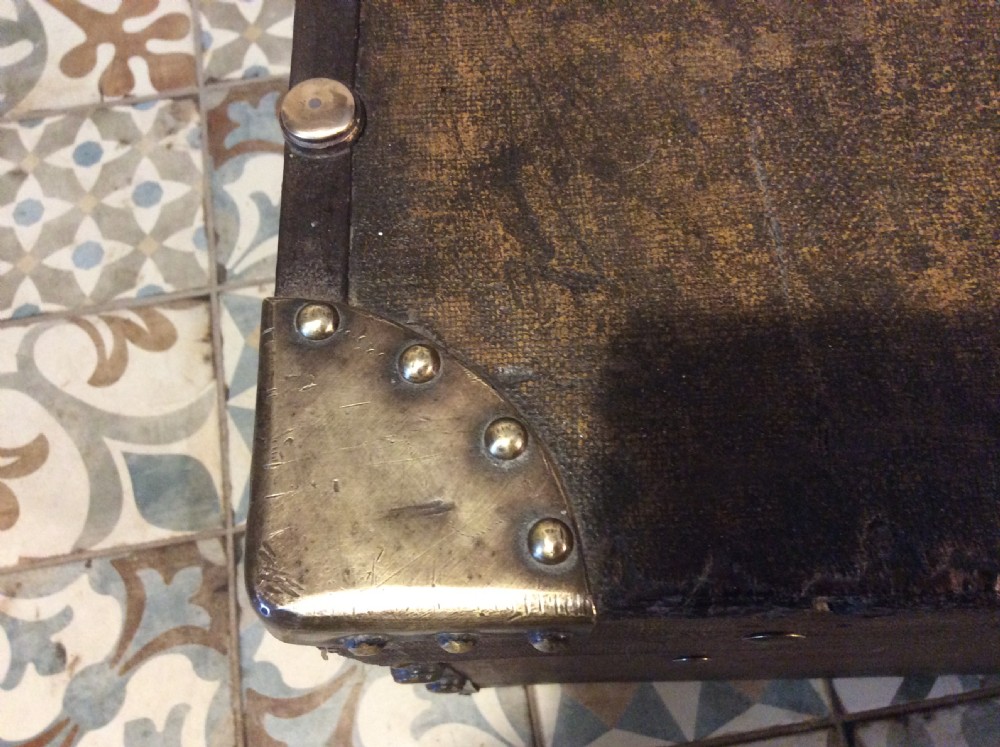 A rectangular Victorian dark brown canvas-covered trunk featuring brass corner caps, brass studs, a central lock, and stencilled black initials on the flat lid. View XV