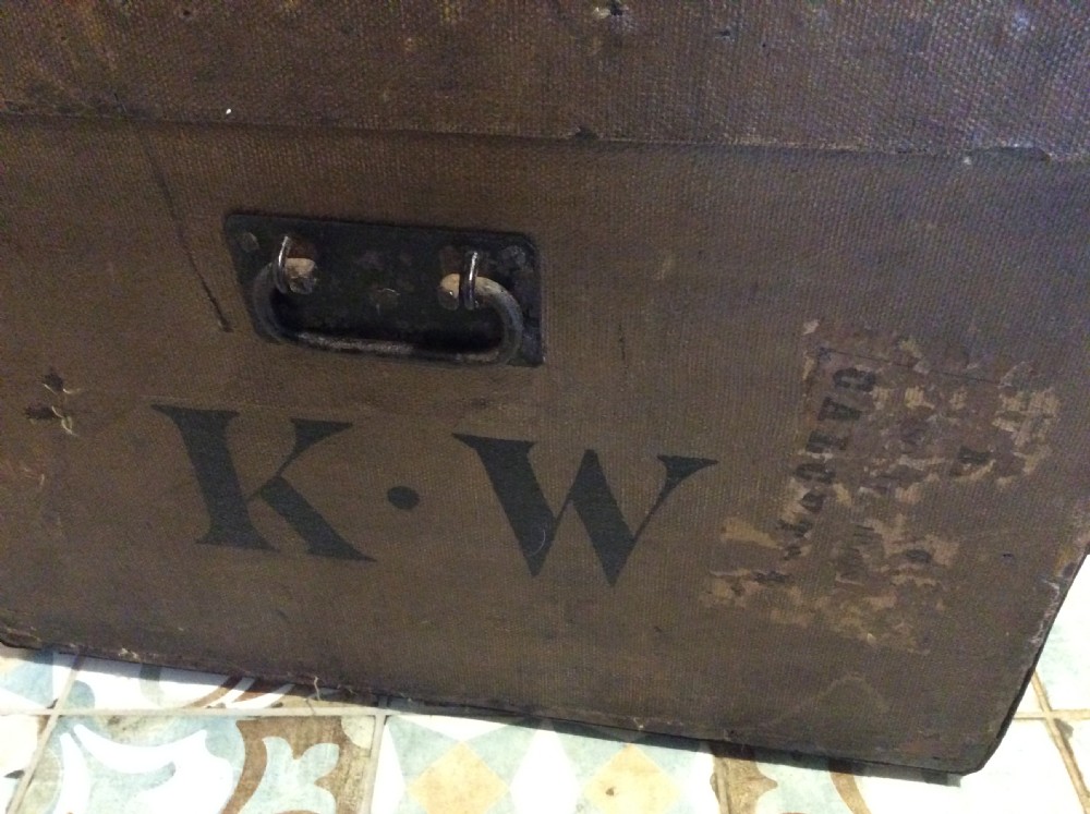 A rectangular Victorian dark brown canvas-covered trunk featuring brass corner caps, brass studs, a central lock, and stencilled black initials on the flat lid. View XVI