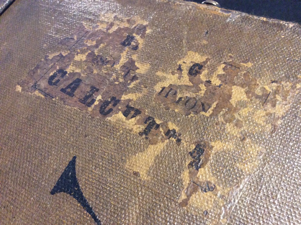 A rectangular Victorian dark brown canvas-covered trunk featuring brass corner caps, brass studs, a central lock, and stencilled black initials on the flat lid. View XVII