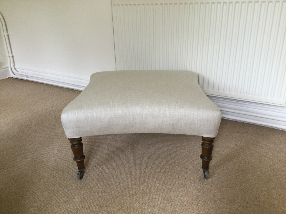 A 19th-century French upholstered footstool featuring cream linen fabric and turned wooden legs fitted with brass castors.