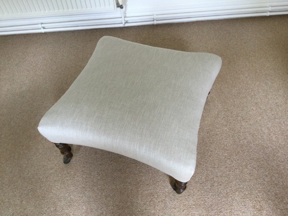 A 19th-century French upholstered footstool featuring cream linen fabric and turned wooden legs fitted with brass castors. View II