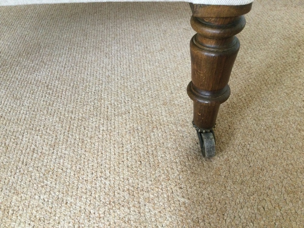 A 19th-century French upholstered footstool featuring cream linen fabric and turned wooden legs fitted with brass castors. View IV