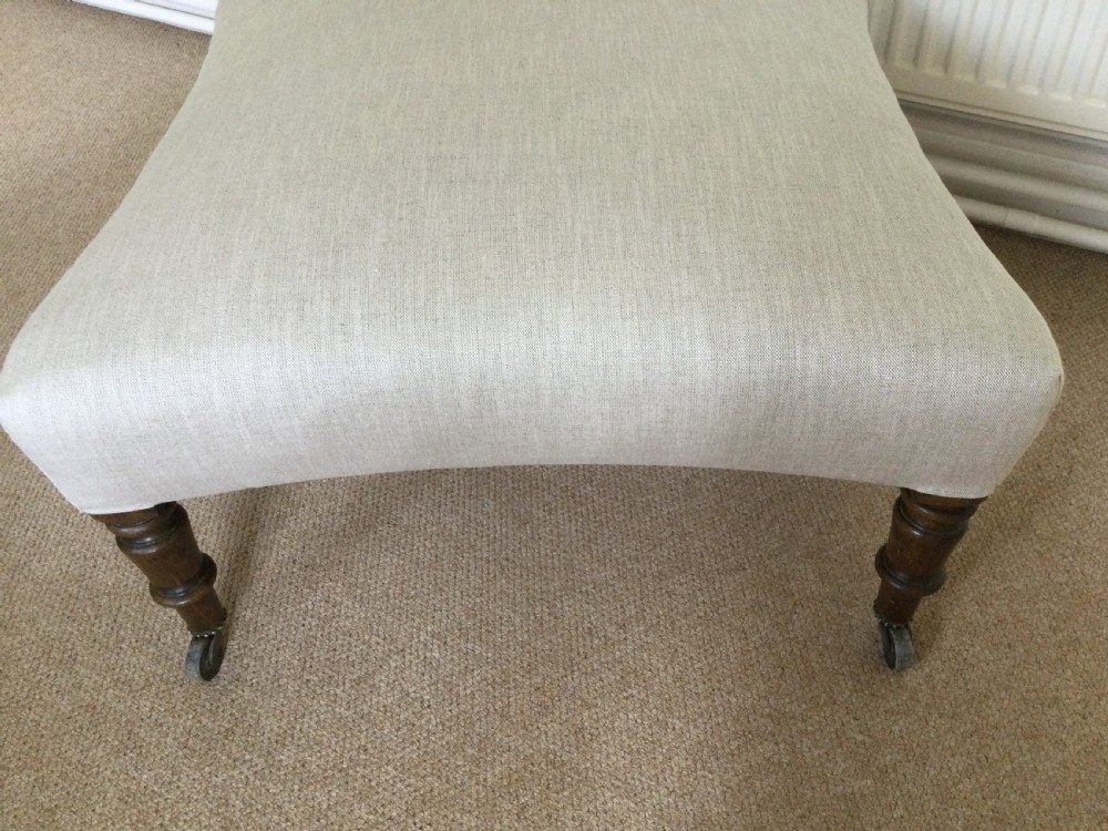 A 19th-century French upholstered footstool featuring cream linen fabric and turned wooden legs fitted with brass castors. View V