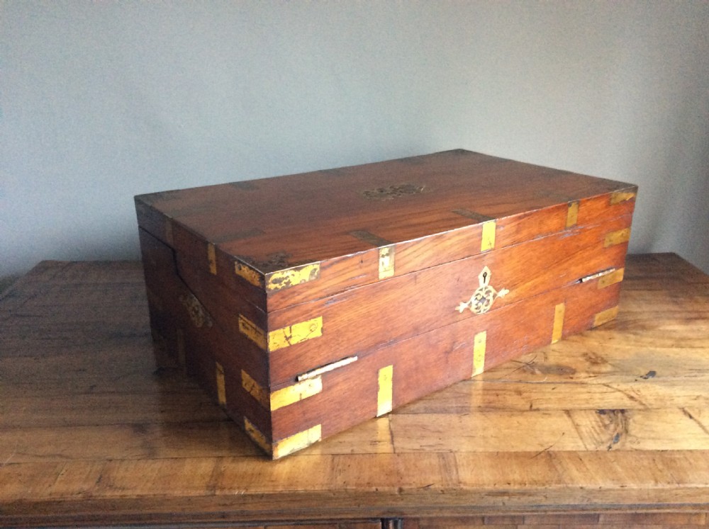 A rectangular warm brown teak campaign writing box featuring flush brass strapwork on the corners and a central decorative brass keyhole escutcheon.