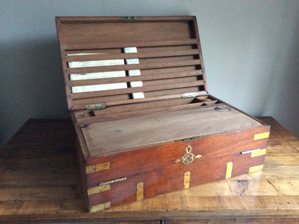 A rectangular warm brown teak campaign writing box featuring flush brass strapwork on the corners and a central decorative brass keyhole escutcheon. View II
