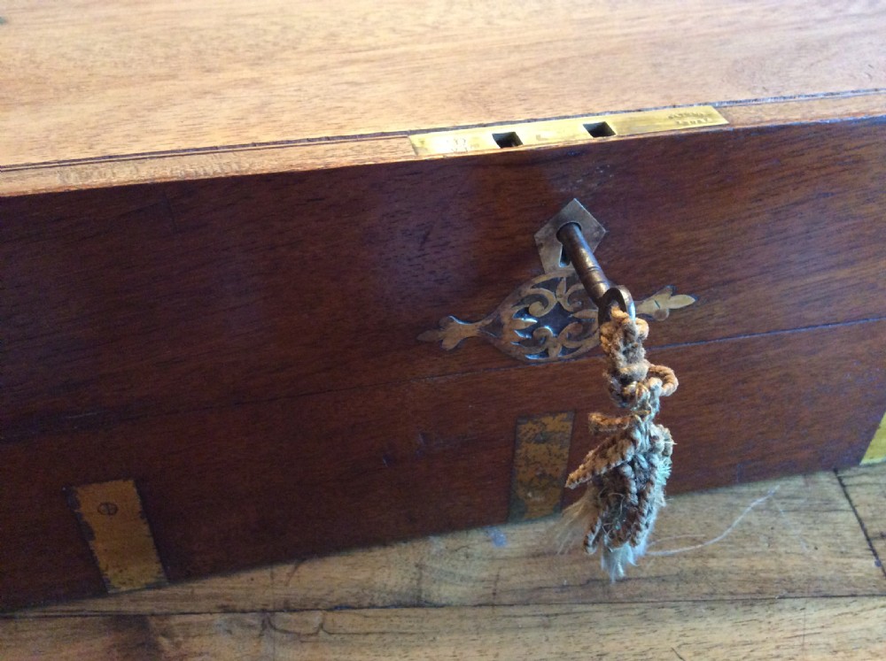 A rectangular warm brown teak campaign writing box featuring flush brass strapwork on the corners and a central decorative brass keyhole escutcheon. View XV