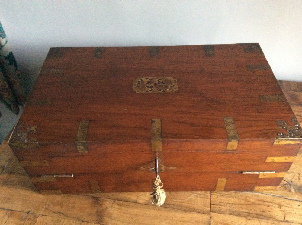 A rectangular warm brown teak campaign writing box featuring flush brass strapwork on the corners and a central decorative brass keyhole escutcheon. View XVI