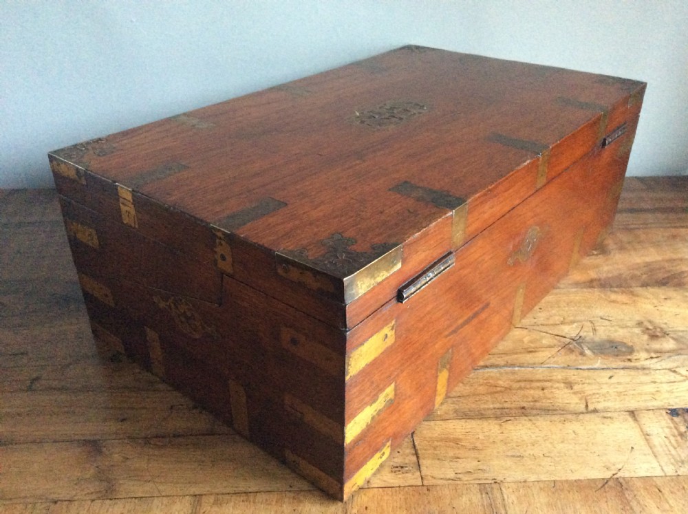 A rectangular warm brown teak campaign writing box featuring flush brass strapwork on the corners and a central decorative brass keyhole escutcheon. View XVIII