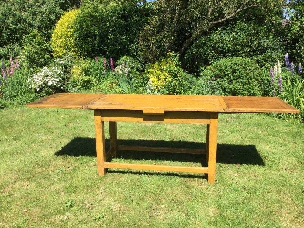 A rectangular warm pine farmhouse kitchen table featuring two end extension leaves supported by a sturdy square-legged stretcher base.