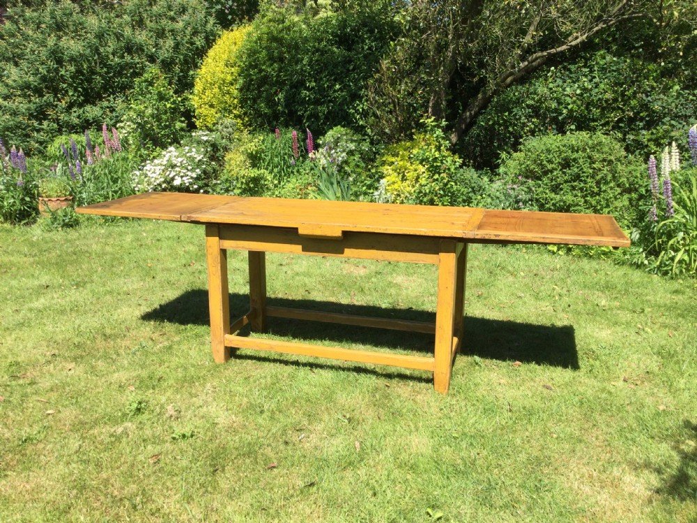 A rectangular warm pine farmhouse kitchen table featuring two end extension leaves supported by a sturdy square-legged stretcher base. View III