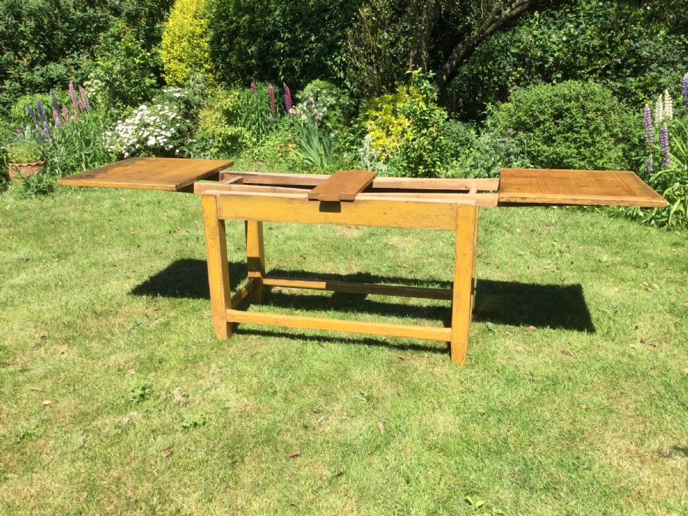 A rectangular warm pine farmhouse kitchen table featuring two end extension leaves supported by a sturdy square-legged stretcher base. View VI
