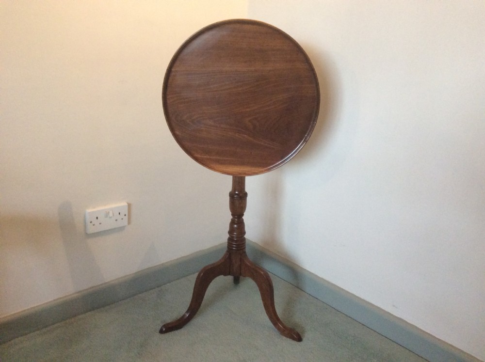 A George III mahogany tilt-top wine table with a circular dished top shown vertically above a turned column and tripod cabriole legs.