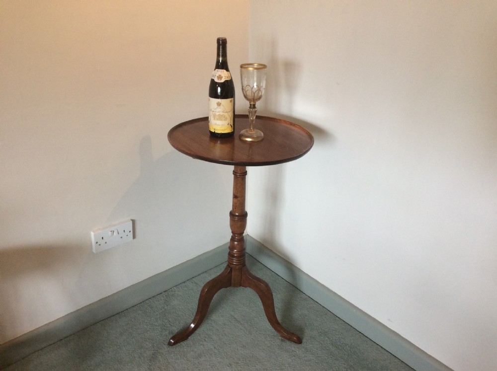 A George III mahogany tilt-top wine table with a circular dished top shown vertically above a turned column and tripod cabriole legs. View II
