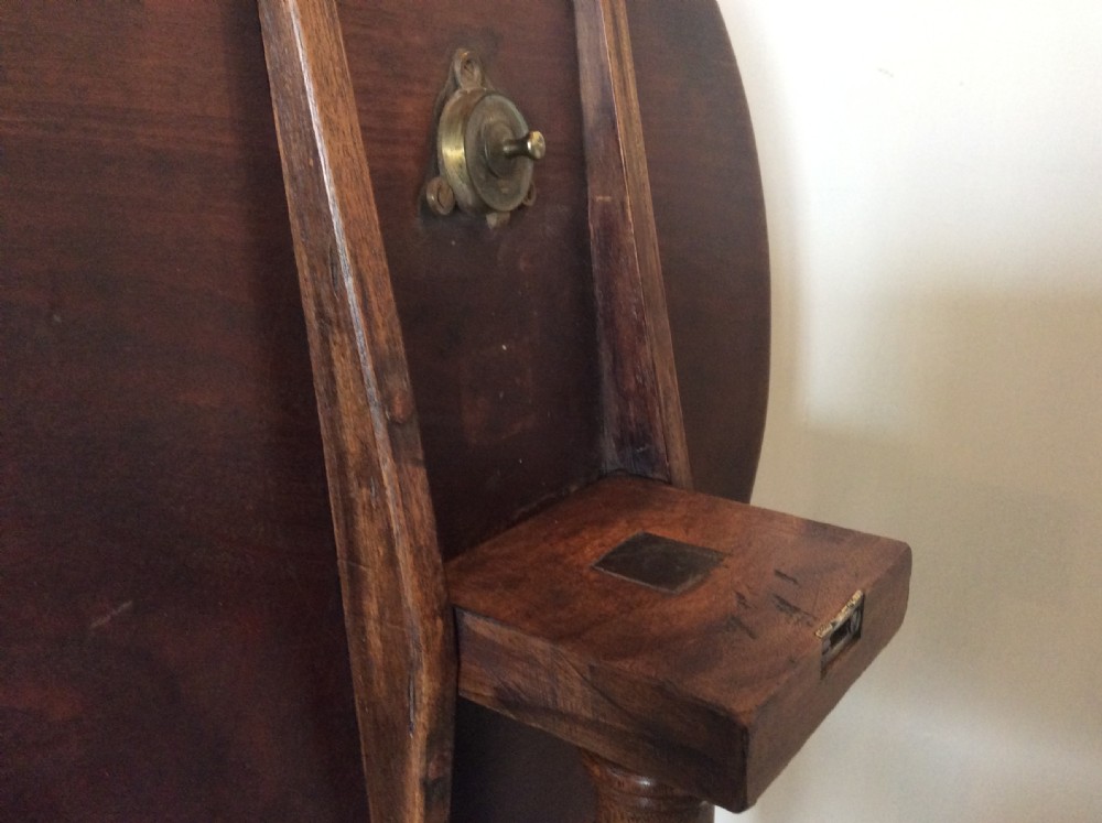A George III mahogany tilt-top wine table with a circular dished top shown vertically above a turned column and tripod cabriole legs. View VI
