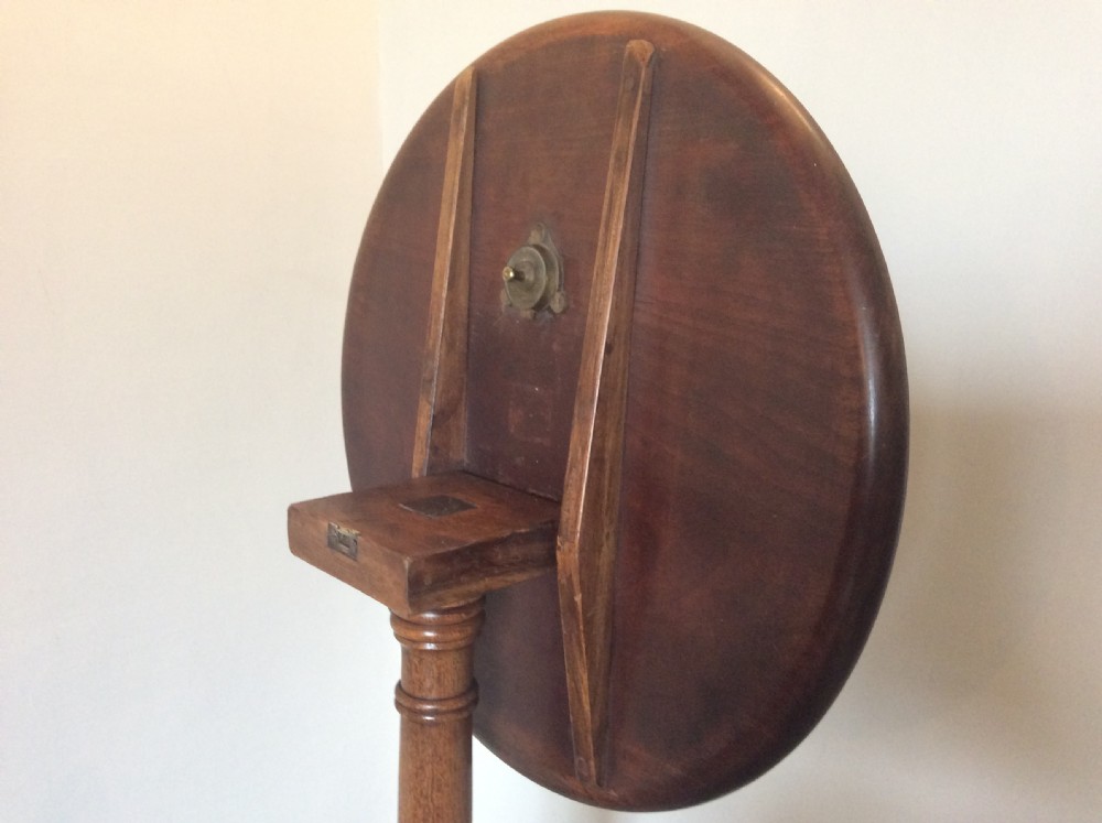 A George III mahogany tilt-top wine table with a circular dished top shown vertically above a turned column and tripod cabriole legs. View VII