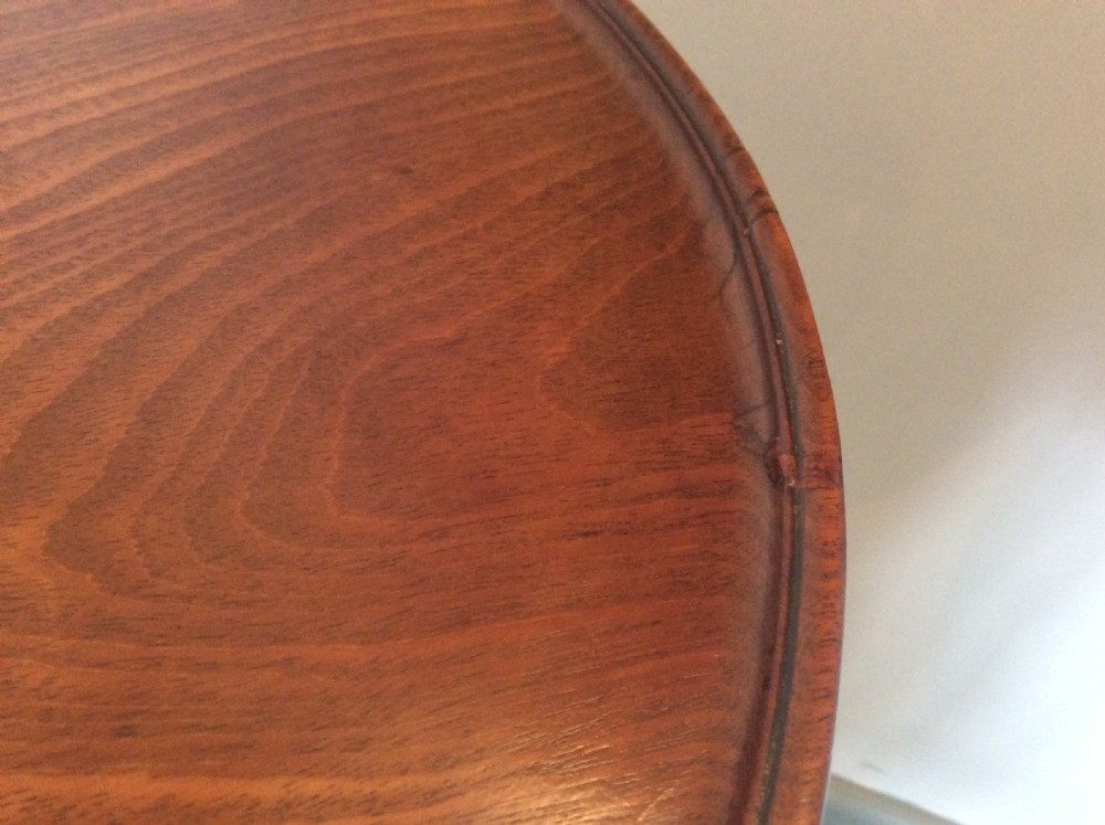 A George III mahogany tilt-top wine table with a circular dished top shown vertically above a turned column and tripod cabriole legs. View X
