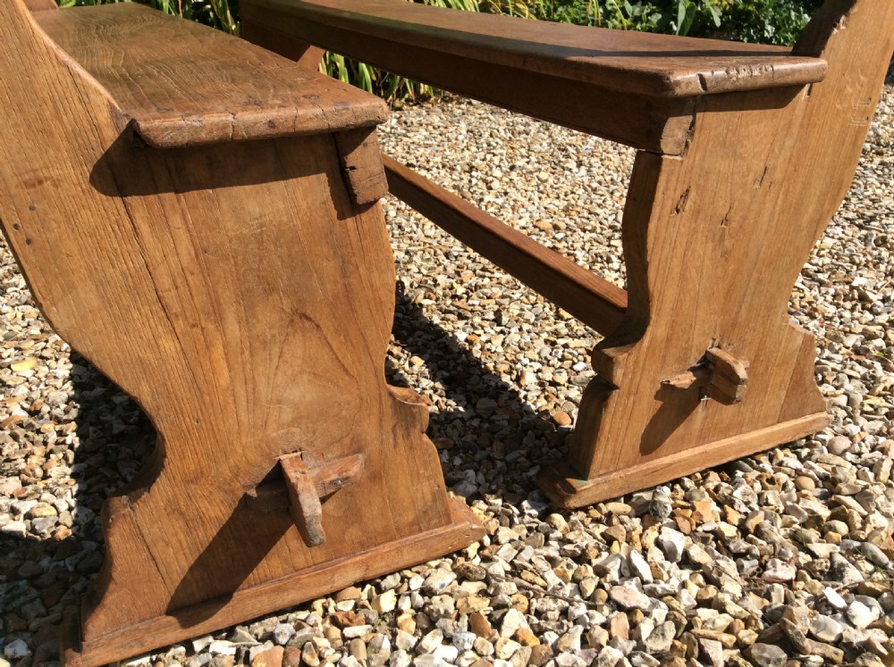 A pair of matching warm brown timber benches featuring low backrests, shaped side supports, and lower stretchers. View III