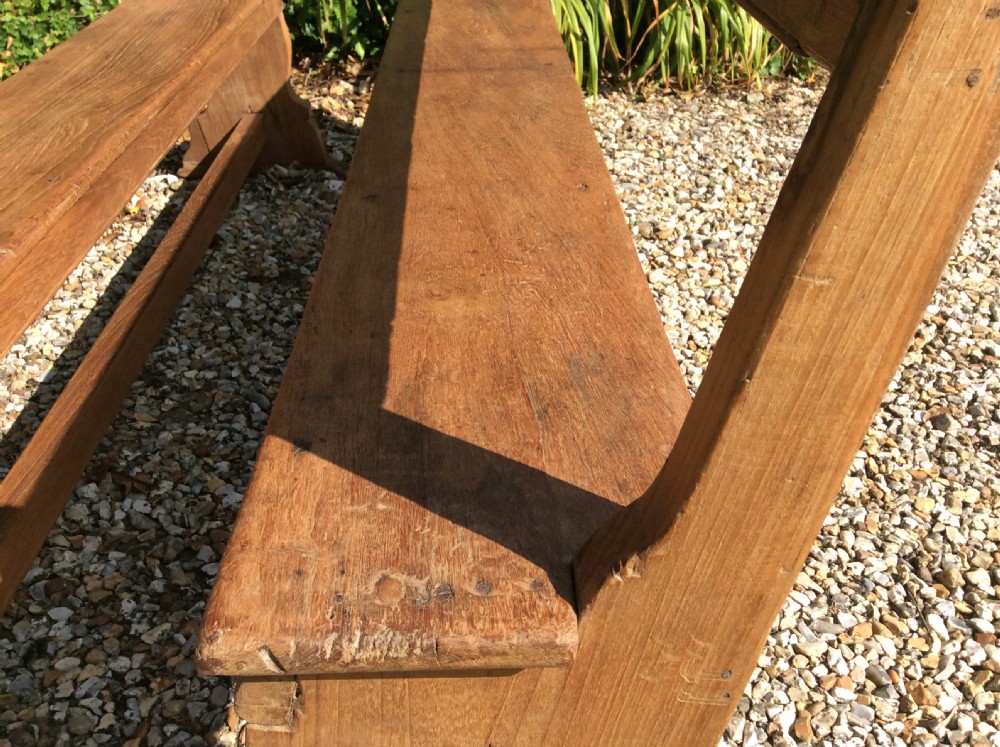 A pair of matching warm brown timber benches featuring low backrests, shaped side supports, and lower stretchers. View V