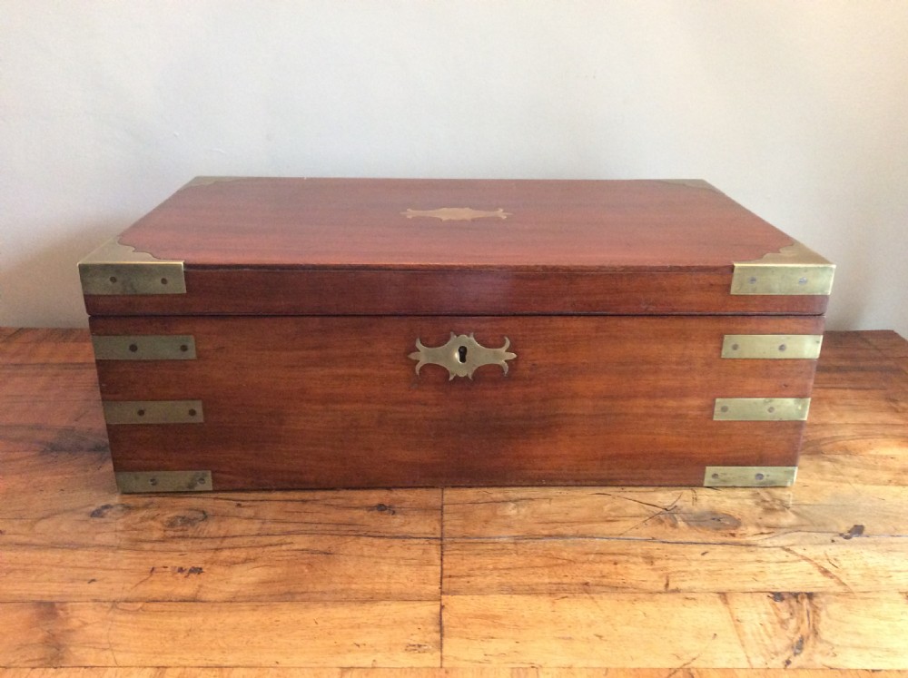 A rectangular mahogany campaign writing slope with flush brass corner brackets, brass straps, and a decorative brass keyhole escutcheon.