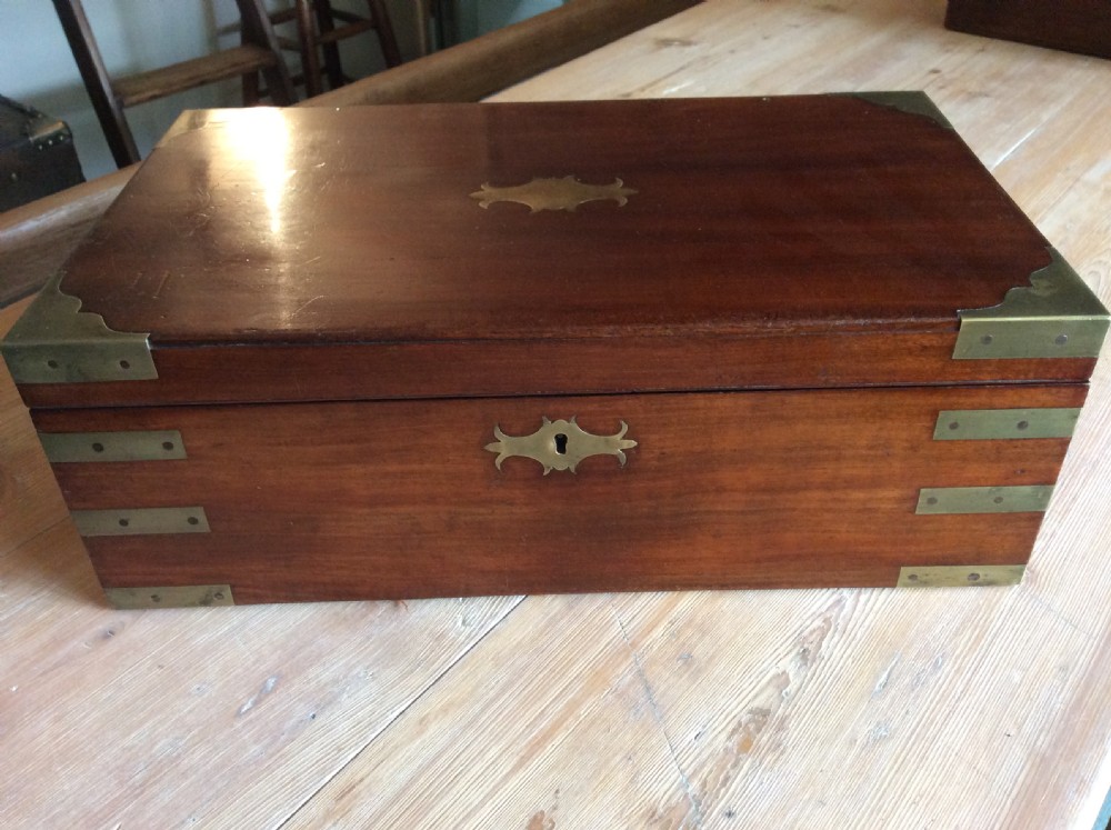A rectangular mahogany campaign writing slope with flush brass corner brackets, brass straps, and a decorative brass keyhole escutcheon. View V
