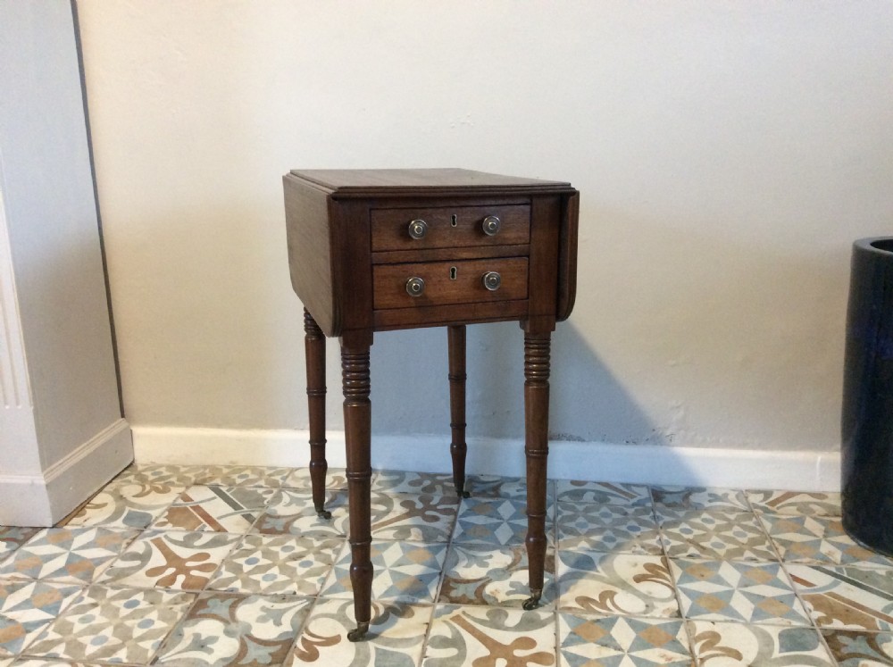 A 19th-century mahogany work table featuring two drawers with circular knobs, double drop leaves, and slender turned legs on brass castors.