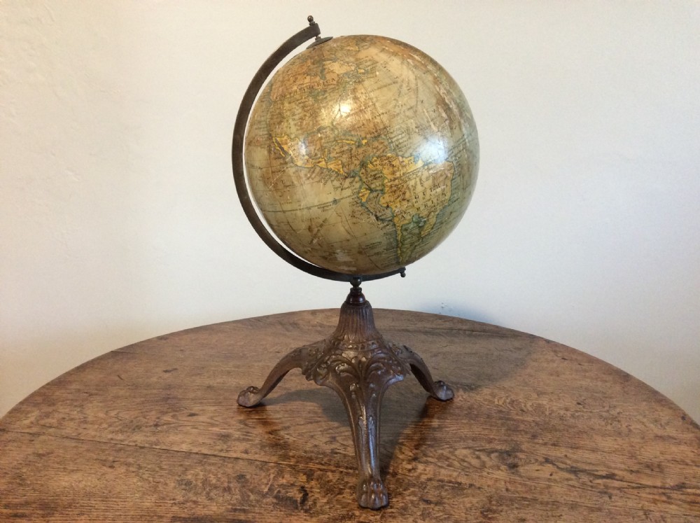 A printed paper terrestrial globe mounted on an ornate cast iron tripod base with a metal semi-meridian arm.