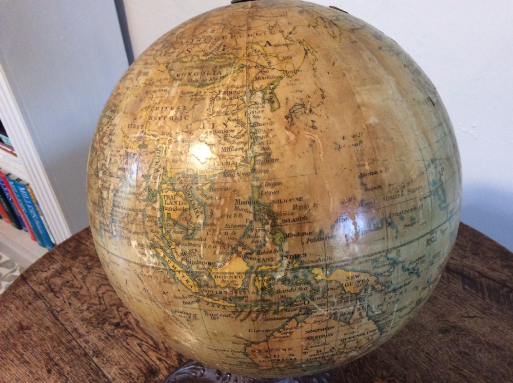 A printed paper terrestrial globe mounted on an ornate cast iron tripod base with a metal semi-meridian arm. View X