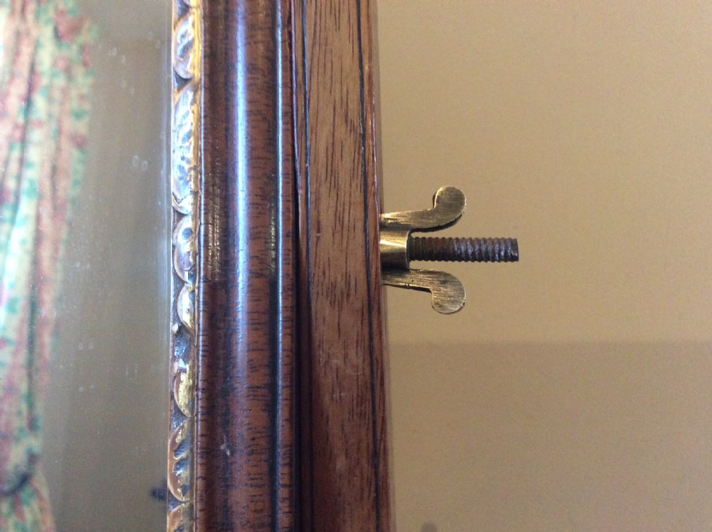 A Georgian dark mahogany skeleton toilet mirror featuring a scroll-carved cresting, rectangular pivoting mirror, side brass fixings, and trestle feet. View IV