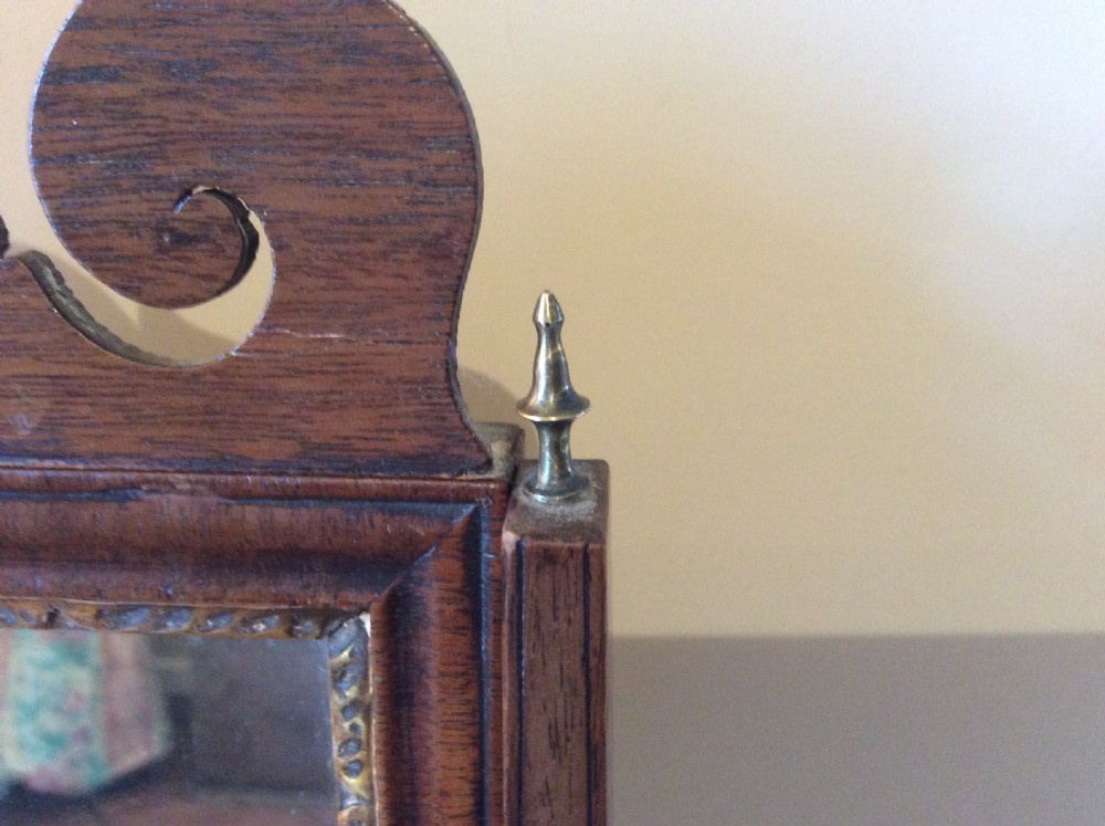 A Georgian dark mahogany skeleton toilet mirror featuring a scroll-carved cresting, rectangular pivoting mirror, side brass fixings, and trestle feet. View V
