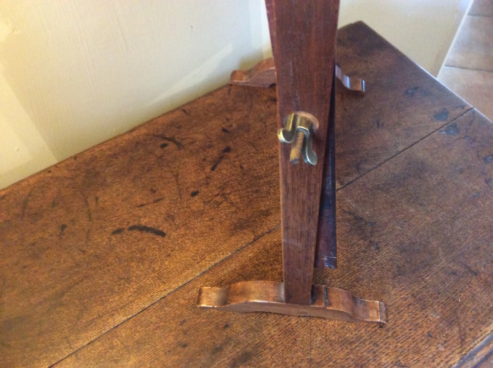 A Georgian dark mahogany skeleton toilet mirror featuring a scroll-carved cresting, rectangular pivoting mirror, side brass fixings, and trestle feet. View VII